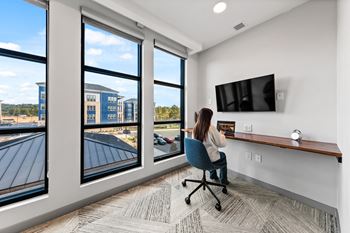 A woman is sitting at a desk in a room with a large window overlooking a parking lot.